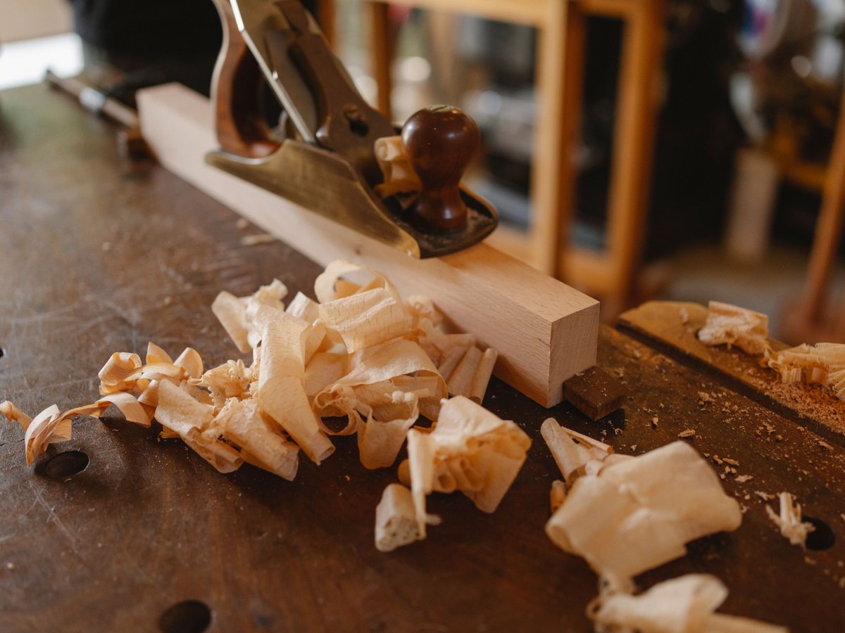 A hand plane resting on a part-finished plank, curls of fresh shavings across the workbench