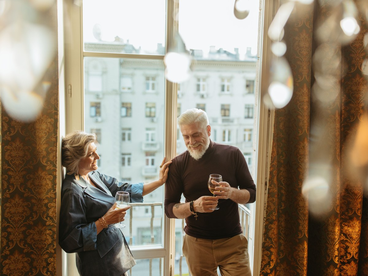 An older couple raising glasses together by open balcony doors