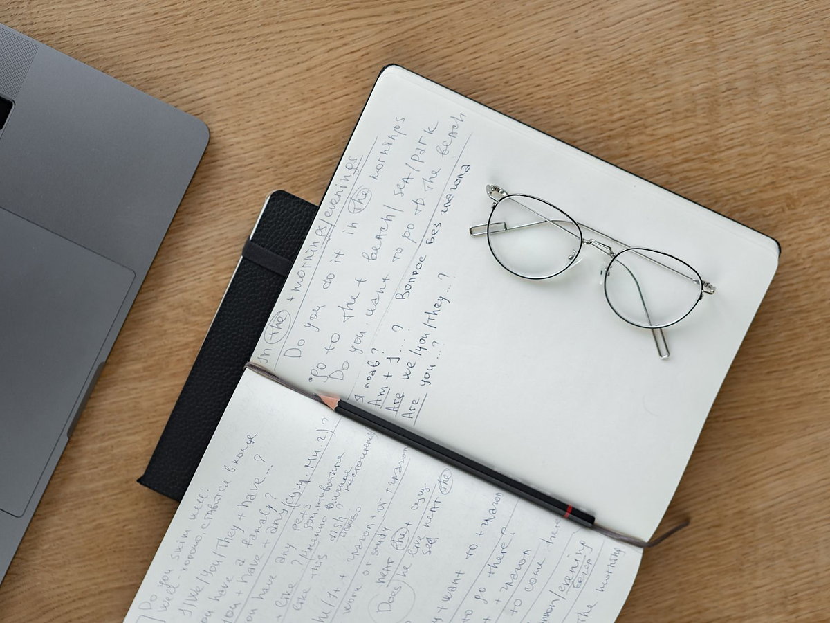 An open planner, reading glasses and a laptop on a desk mid-planning