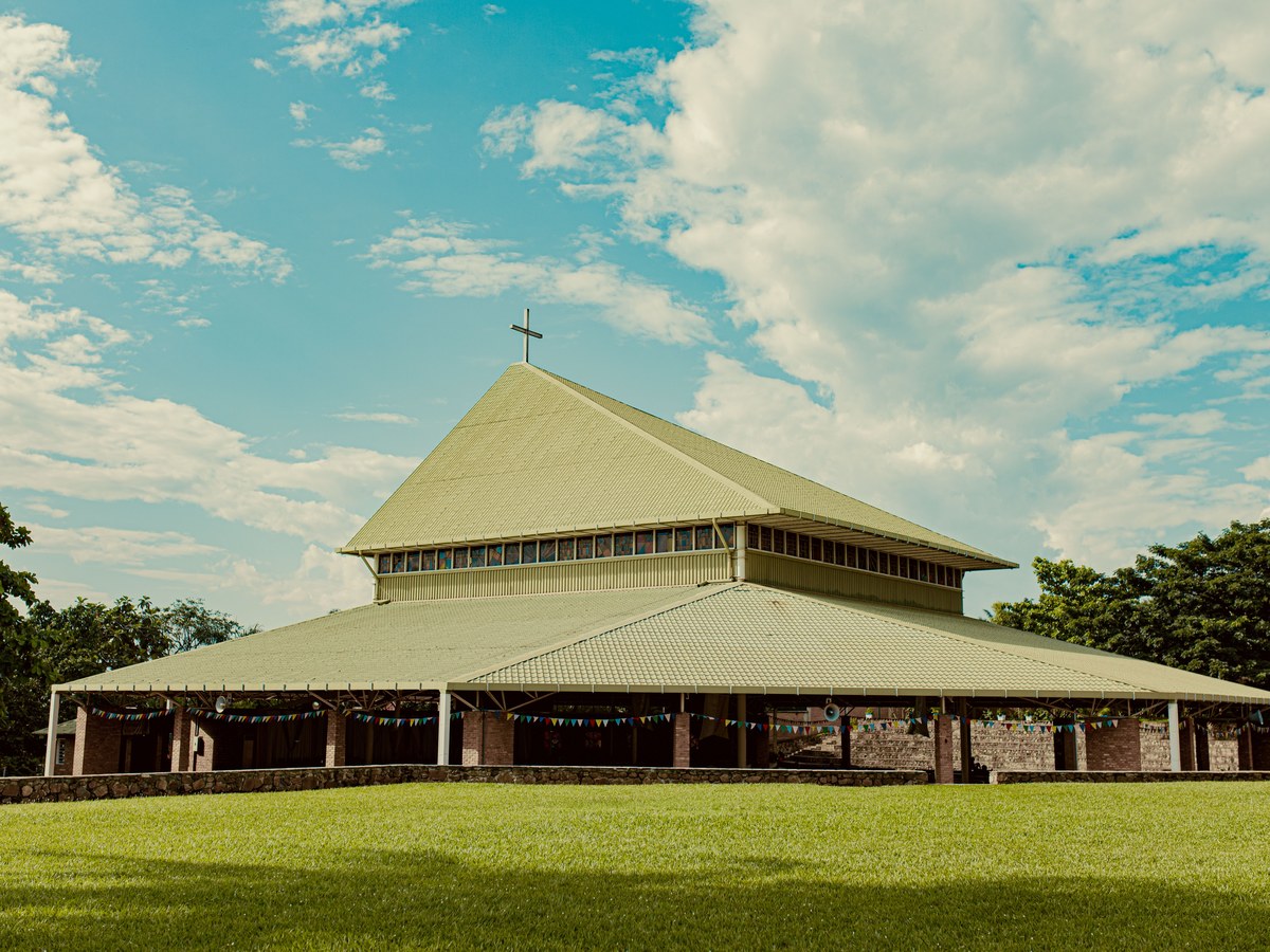 A large church with a cross on its ridge, standing over a clipped green lawn under a bright sky